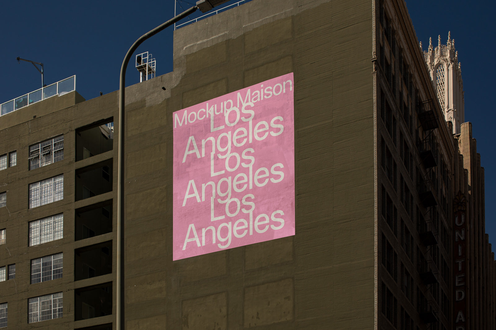 PSD mockup of a pink poster on a building featuring repeated text "Los Angeles" in white, set against a clear blue sky.