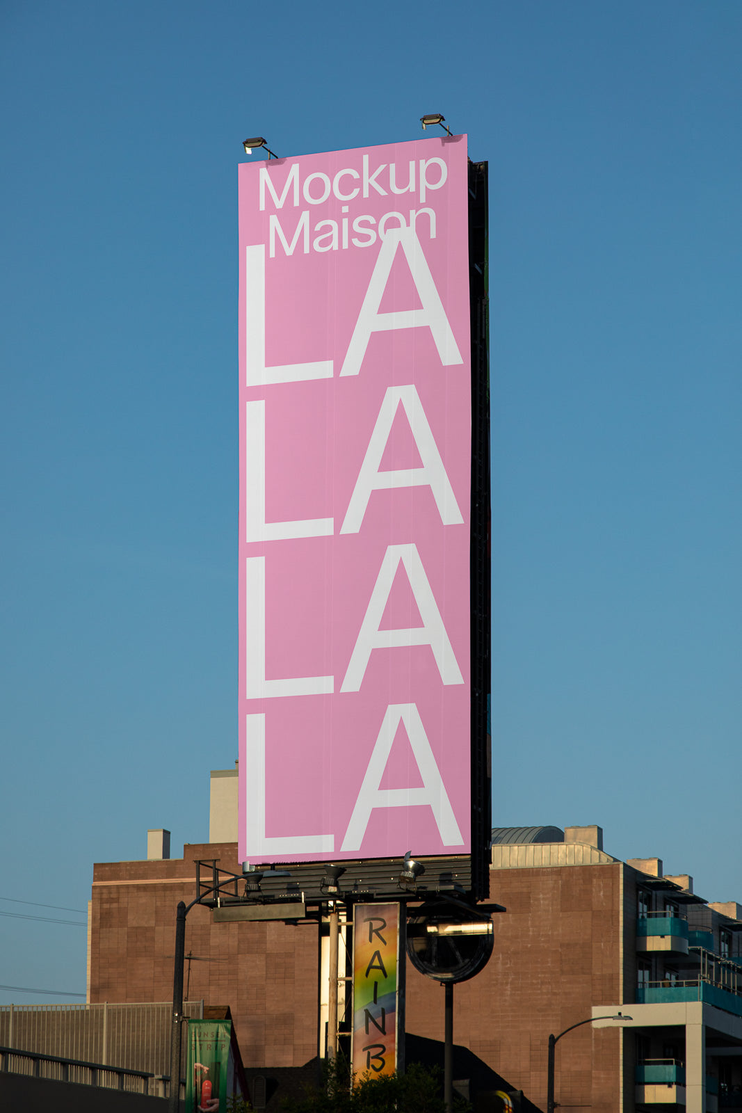 PSD mockup of a tall, pink billboard with white text reading "Mockup Maison LALALA" against a clear blue sky, set in an urban environment.