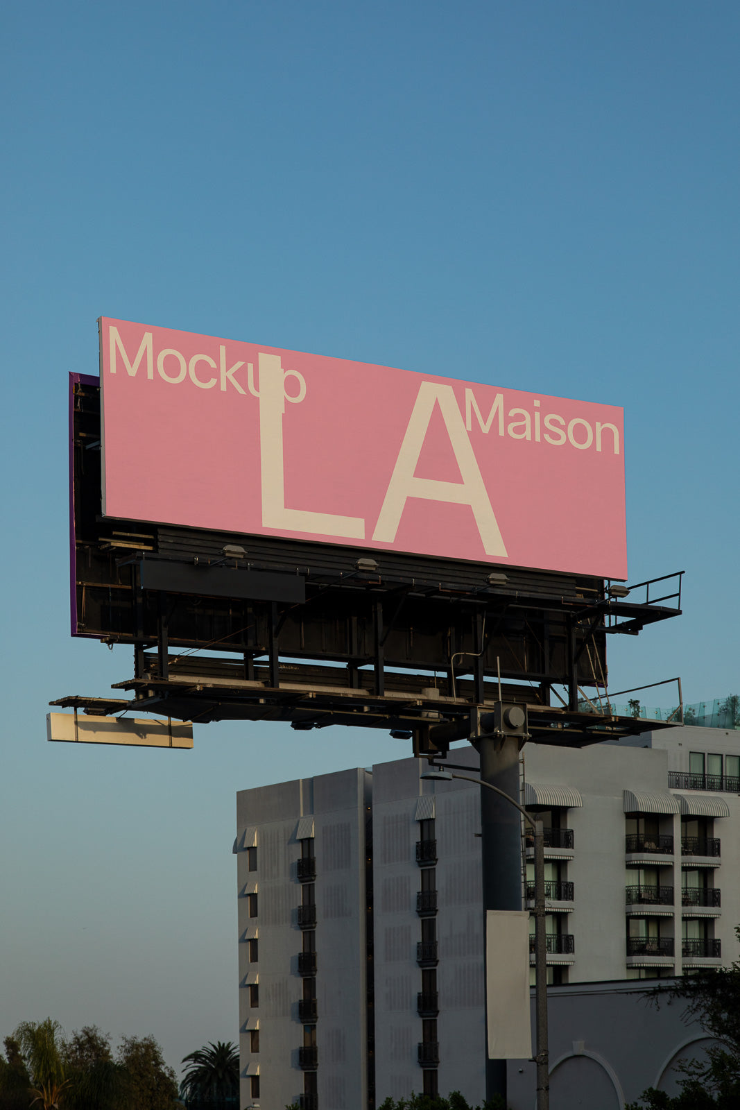 PSD mockup of a large pink billboard displaying the text "Mockup LA Maison" against a clear blue sky, with a modern building in the background.
