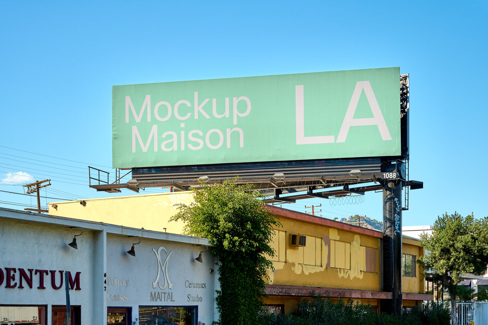 PSD mockup of a large billboard displaying the words "Mockup Maison LA" above a pottery and ceramics studio, set against a clear blue sky.
