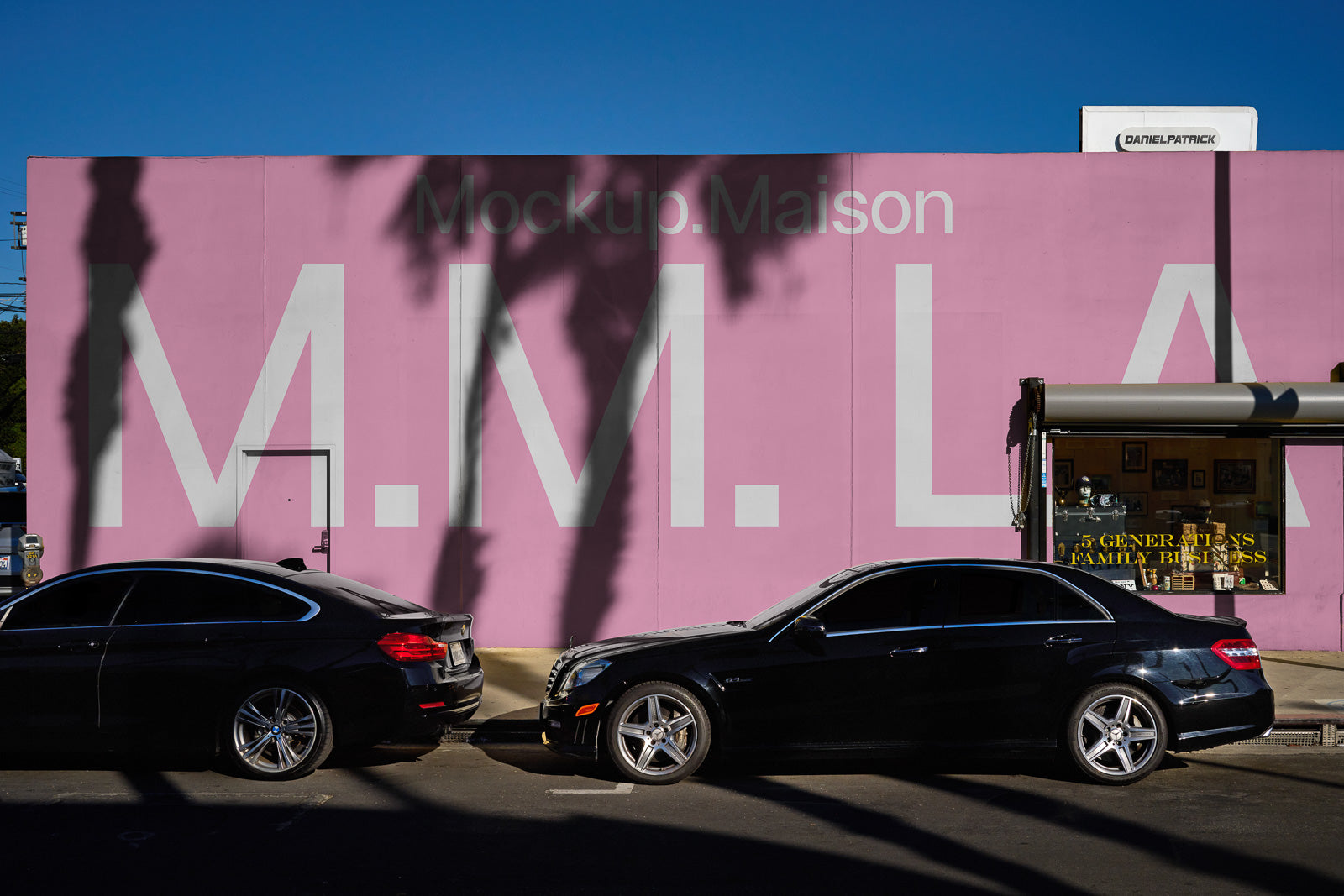 PSD mockup of a pink wall with large "M.M. LA" text in white, casting shadows from nearby palm trees, with two parked black cars in front.