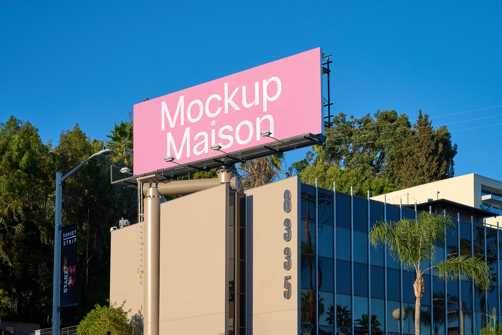 PSD mockup of a large outdoor billboard displaying "Mockup Maison" on a pink background, set against a building with a reflective glass facade and surrounded by trees.