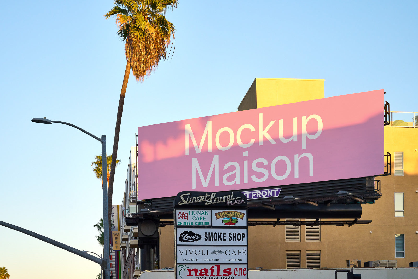 PSD mockup of a pink billboard with text "Mockup Maison" above a street lined with businesses under a clear blue sky.
