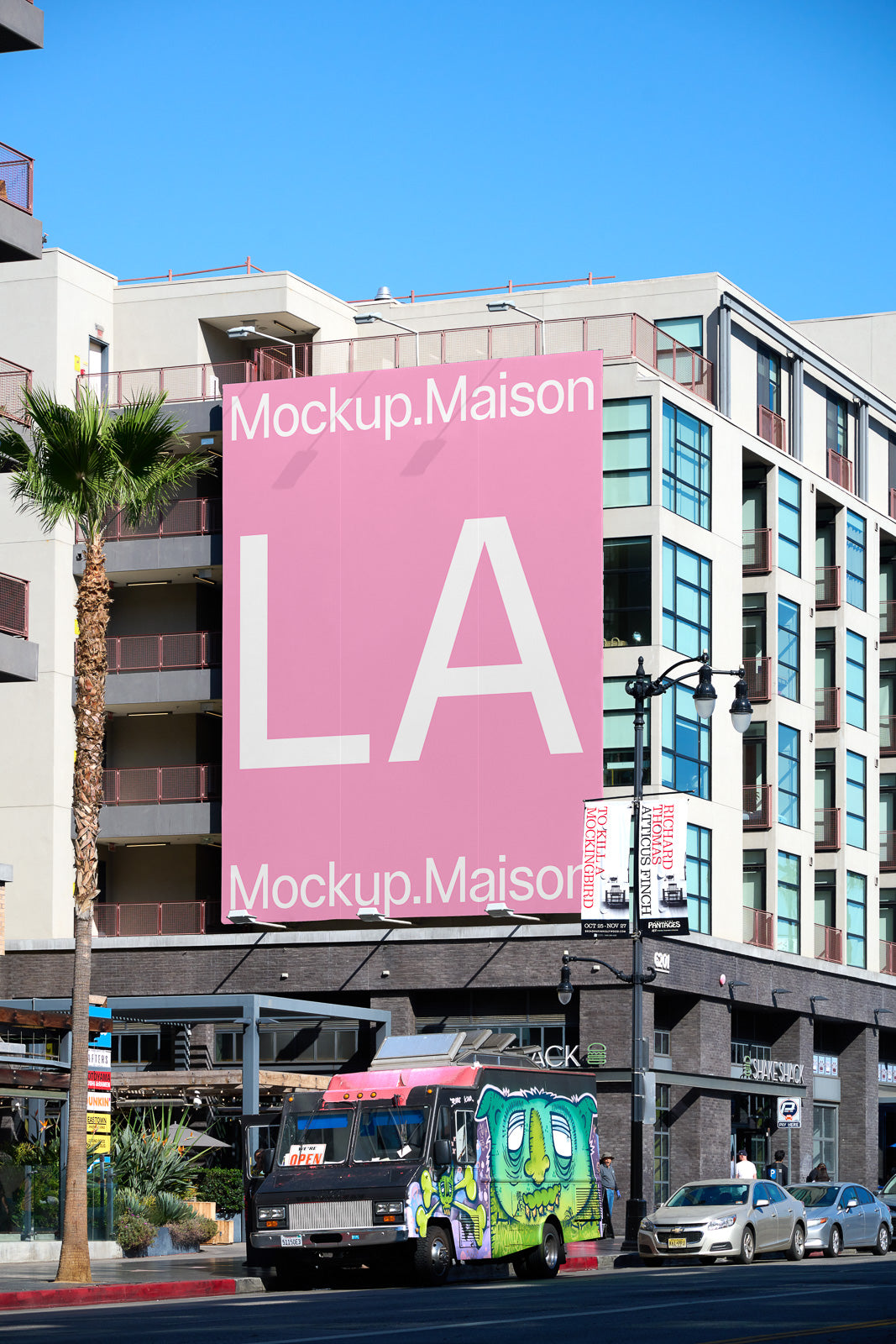 PSD mockup of a large pink billboard on an urban building, displaying "Mockup.Maison" and "LA" with a food truck parked below on a sunny day.