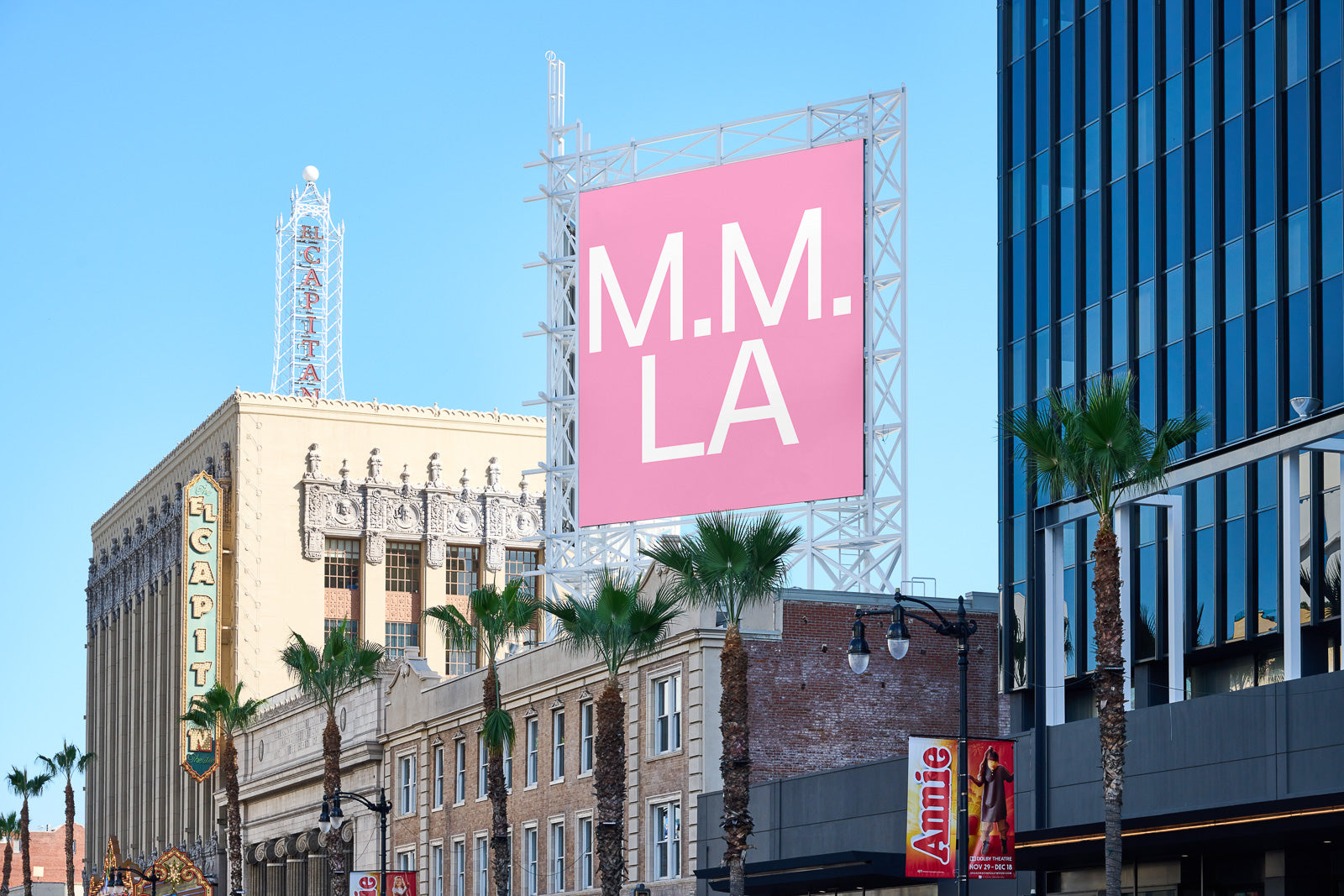 PSD mockup of a pink billboard displaying "M.M. LA" in bold white letters, set against a backdrop of city buildings and palm trees under a clear blue sky.