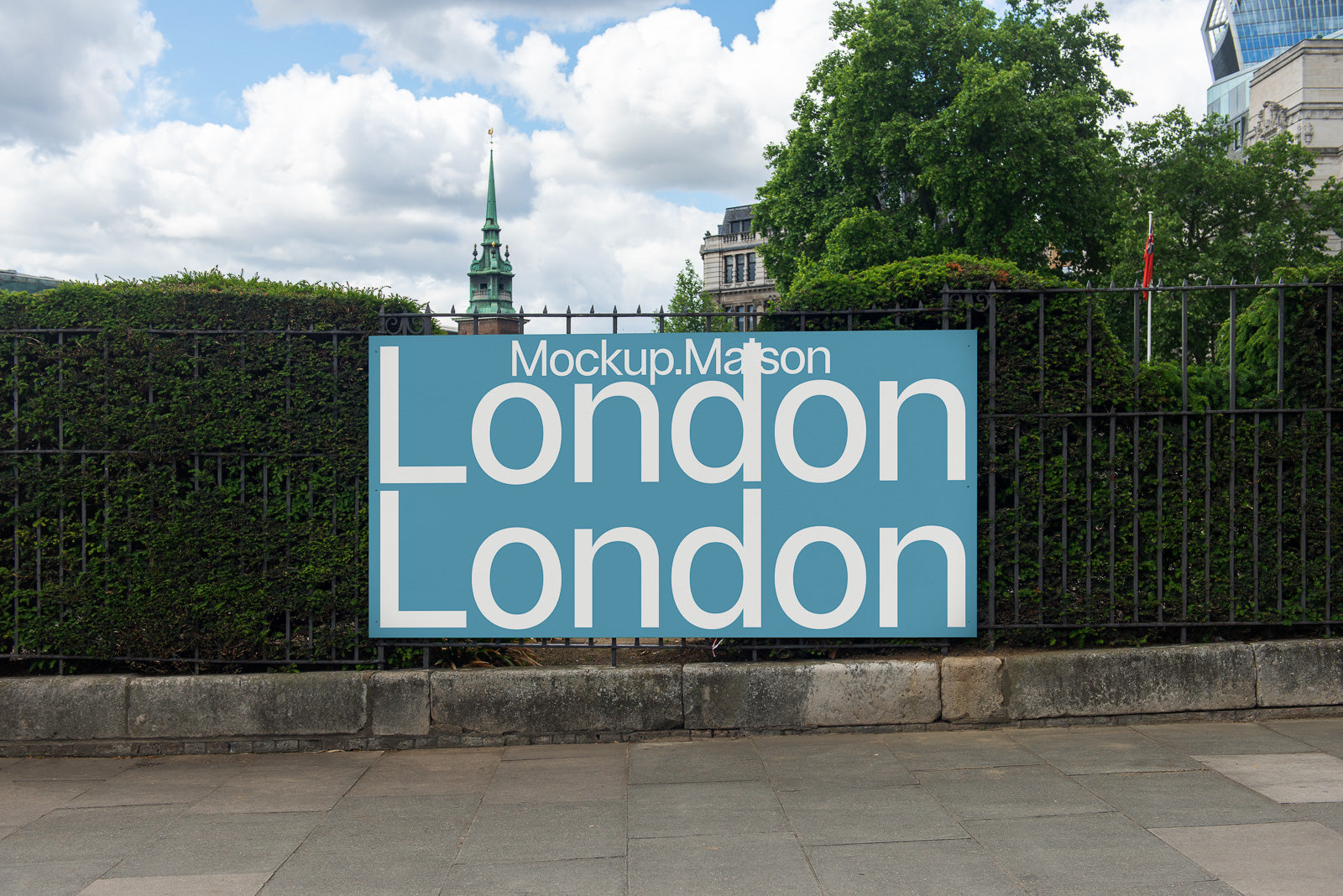 PSD mockup of a large outdoor sign displaying "London" twice, mounted on a metal fence with greenery, buildings, and a cloudy sky in the background.