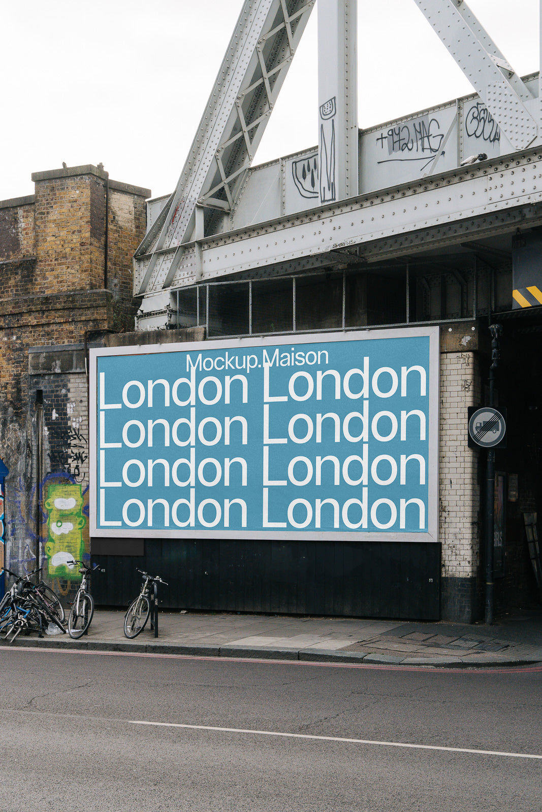 PSD mockup of a large urban billboard displaying the word "London" repeatedly in bold white text on a blue background, situated under a graffitied bridge.
