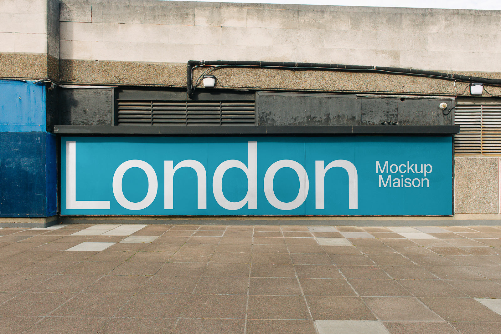 PSD mockup of a large blue wall panel displaying the word "London" in white font next to the text "Mockup Maison" against an urban backdrop.