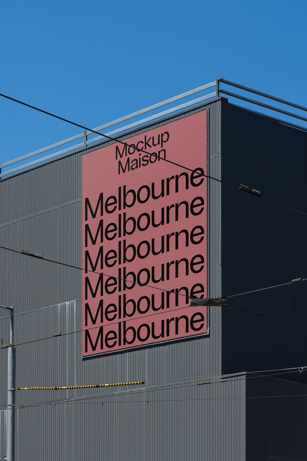 PSD mockup of a large warehouse exterior featuring a vertical pink billboard with repeating text "Melbourne" against a clear blue sky background.