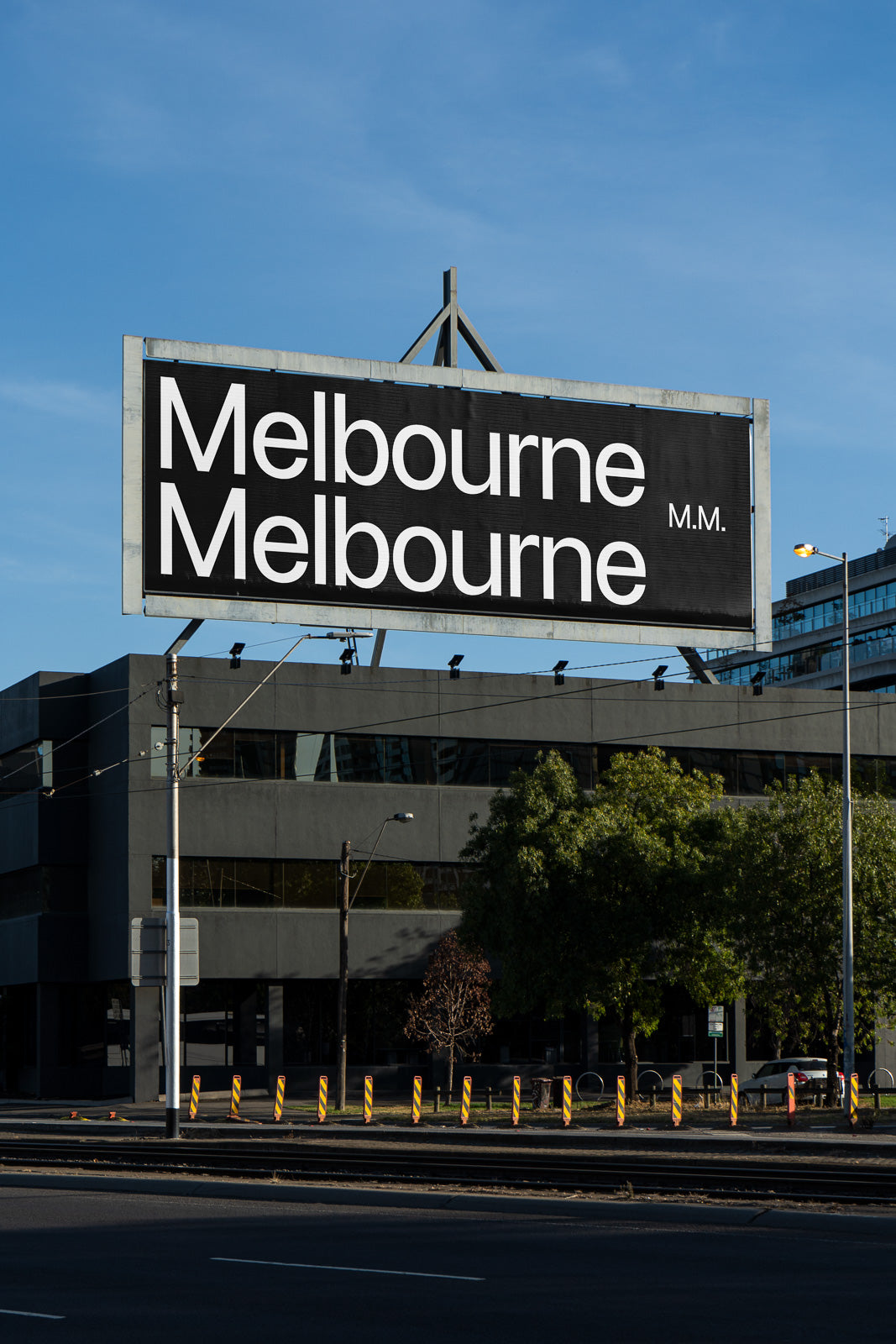 PSD mockup of a large billboard displaying the text "Melbourne" twice in bold white letters on a black background, situated in an urban environment.