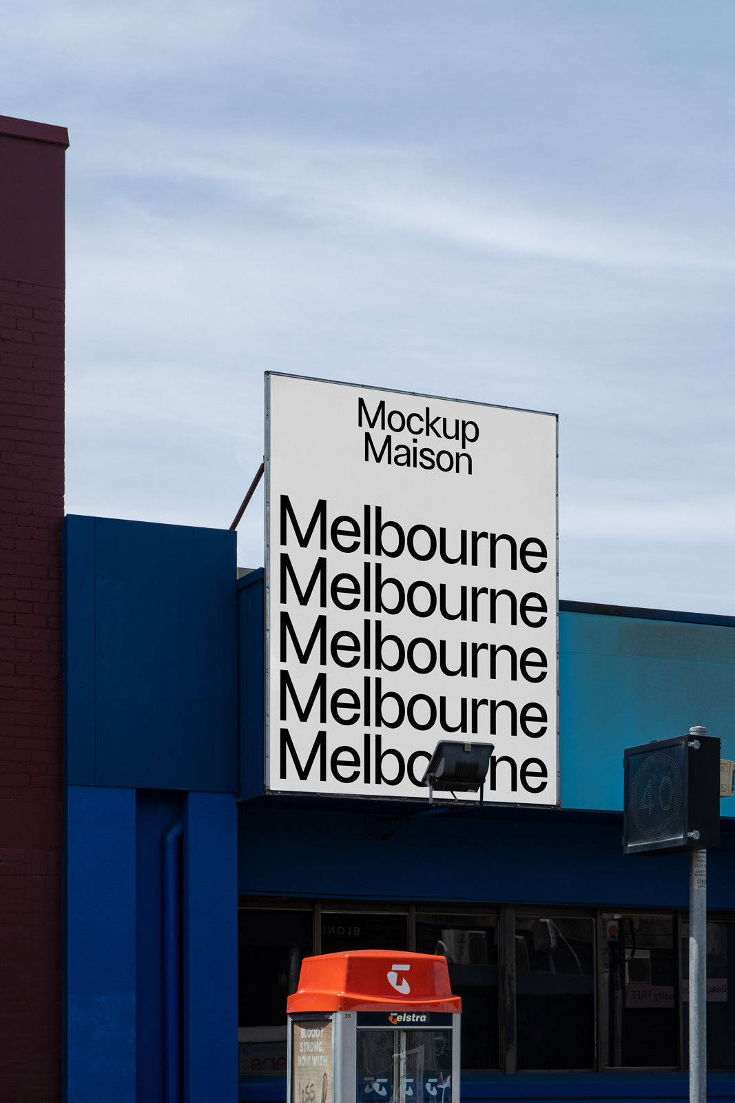 PSD mockup of a large outdoor billboard displaying repetitive text "Melbourne" under "Mockup Maison," set against a blue building with a red phone booth nearby.