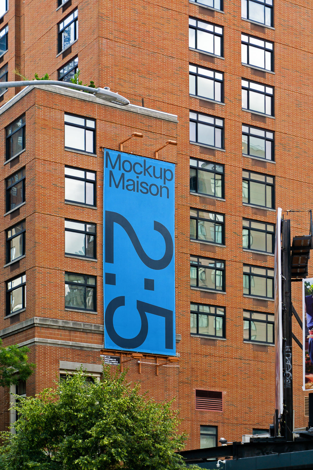 PSD mockup of a large blue banner on a brick building facade, featuring the text "Mockup Maison 2:5" with windows and greenery visible around.