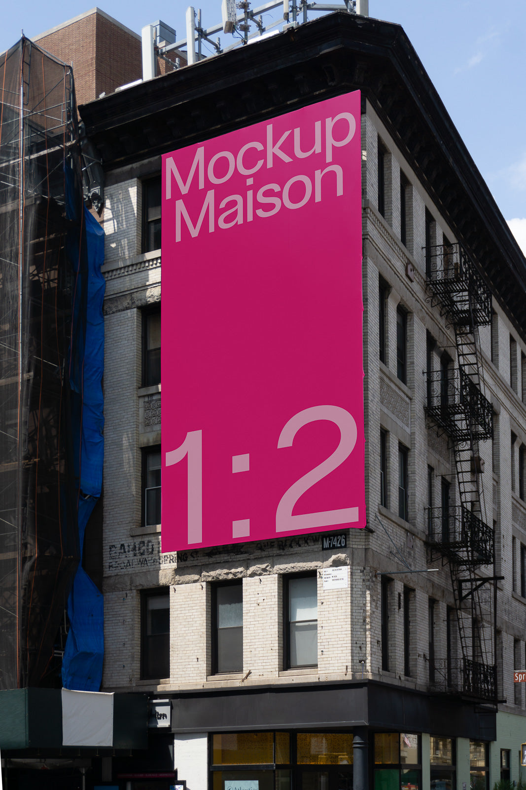 PSD mockup of a large, pink advertisement banner on an urban building facade, displaying the text "Mockup Maison 1:2" against a clear sky.