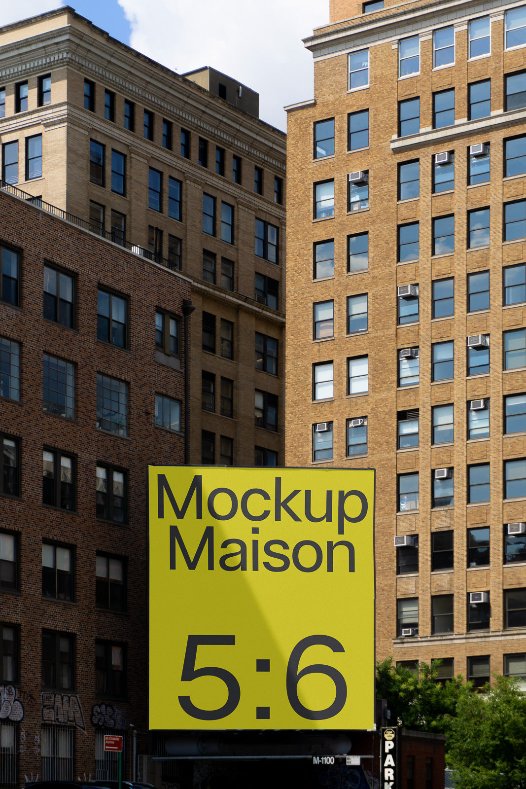 PSD mockup of a large yellow billboard displaying "Mockup Maison 5:6" set against urban brick and stone buildings under a blue sky.