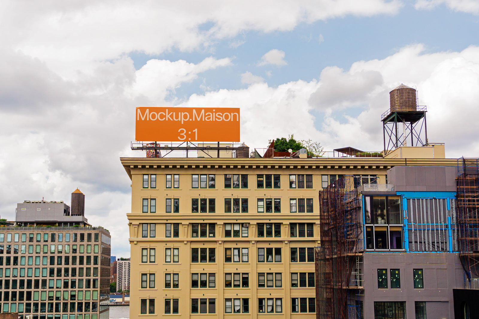 PSD mockup of an urban rooftop scene featuring a large orange billboard displaying "Mockup.Maison 3:1," positioned against a partly cloudy sky.