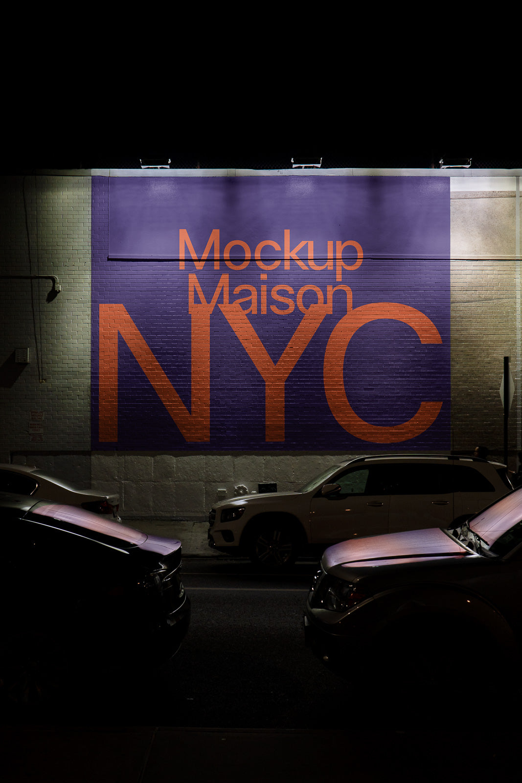 PSD mockup of a large purple mural with orange text "Mockup Maison NYC" on a brick wall, viewed at night with parked cars below.