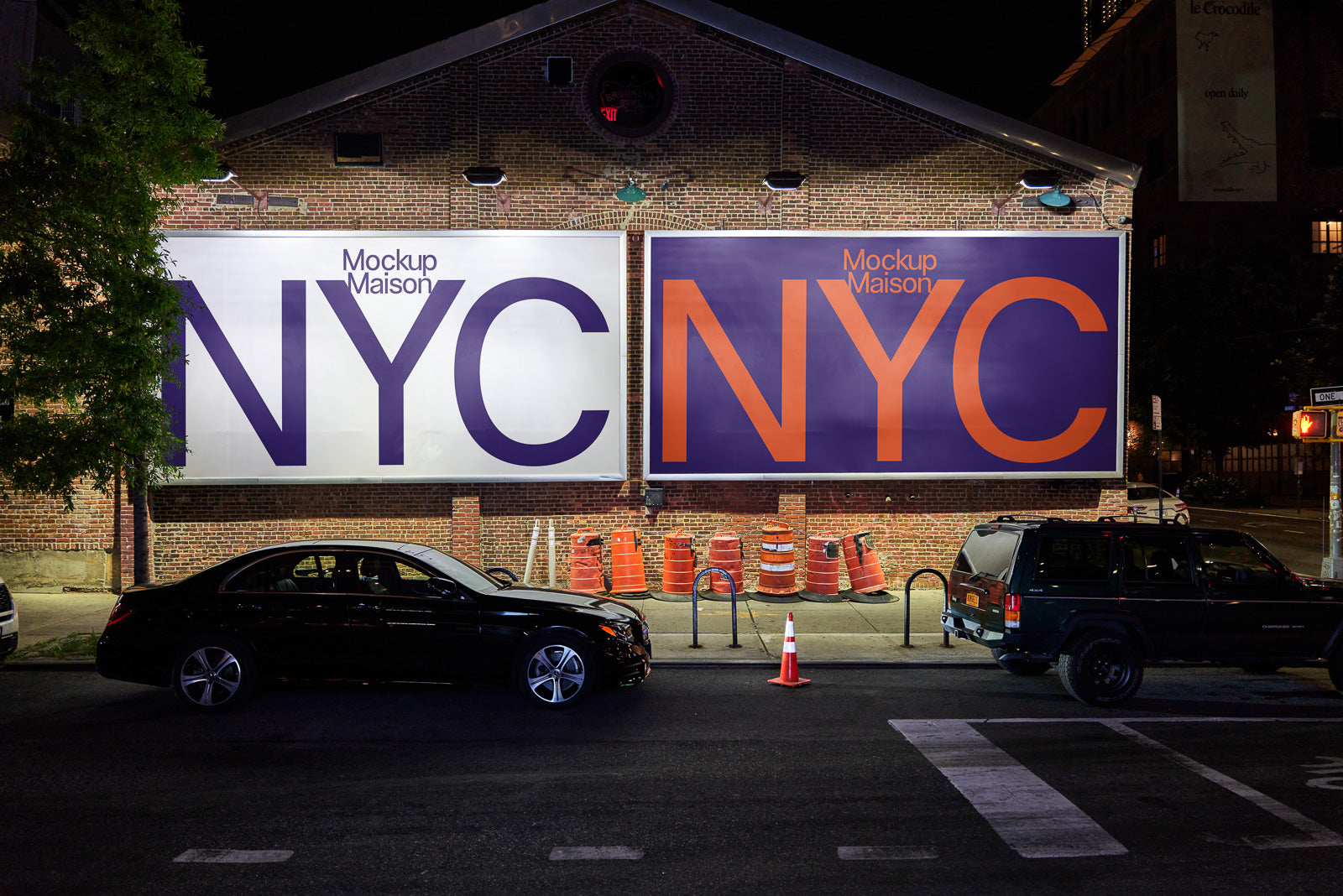 "PSD mockup of two large NYC street billboards on a brick building at night, with parked cars and orange cones in the foreground."