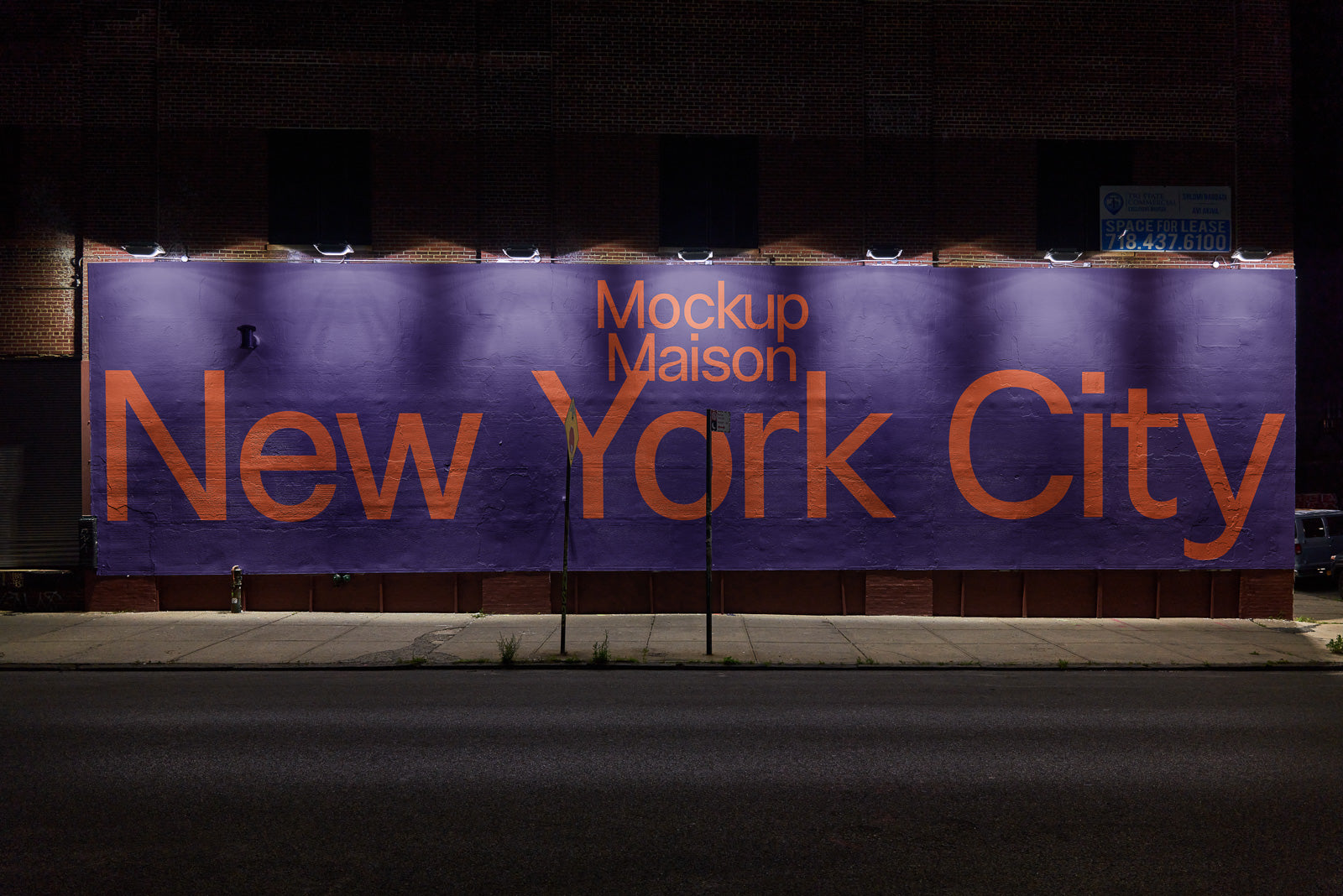 PSD mockup of a large urban wall featuring bold orange text "New York City" with "Mockup Maison" above, set against a purple background and lit by overhead lights.