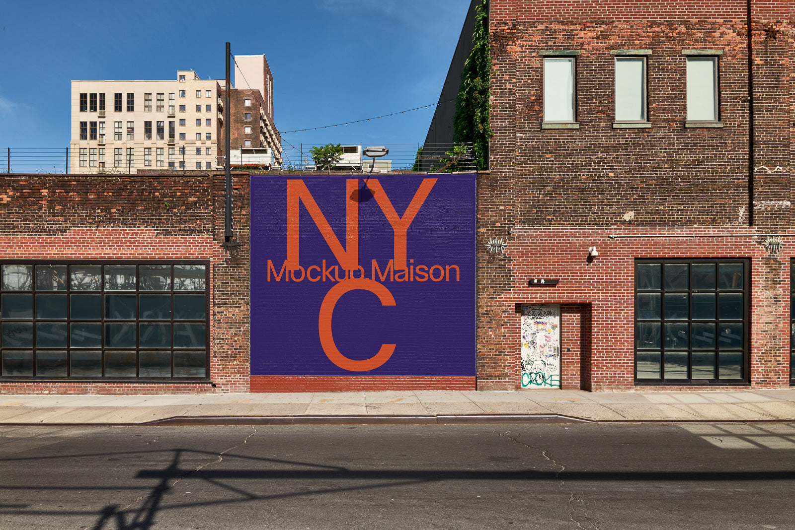PSD mockup of a brick building facade with a large purple mural featuring the text "NYC Mockup Maison" in bold orange letters.
