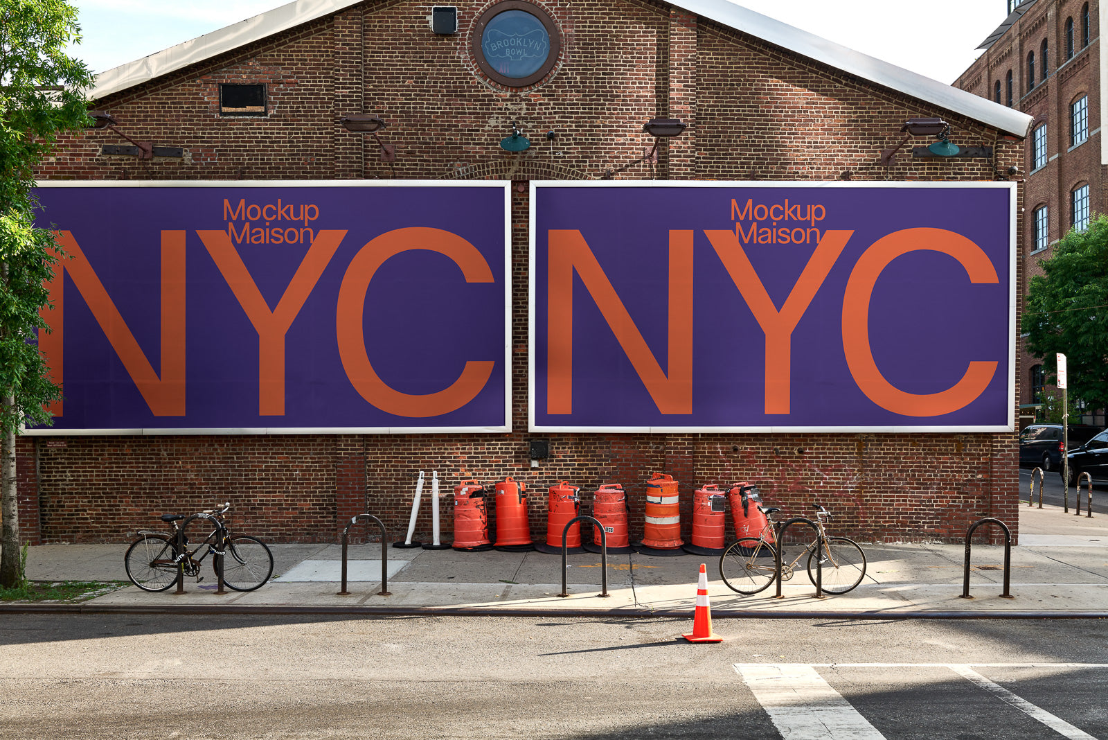PSD mockup of two large purple billboards with orange "NYC" text on a brick building facade, with bicycles and traffic cones in front.