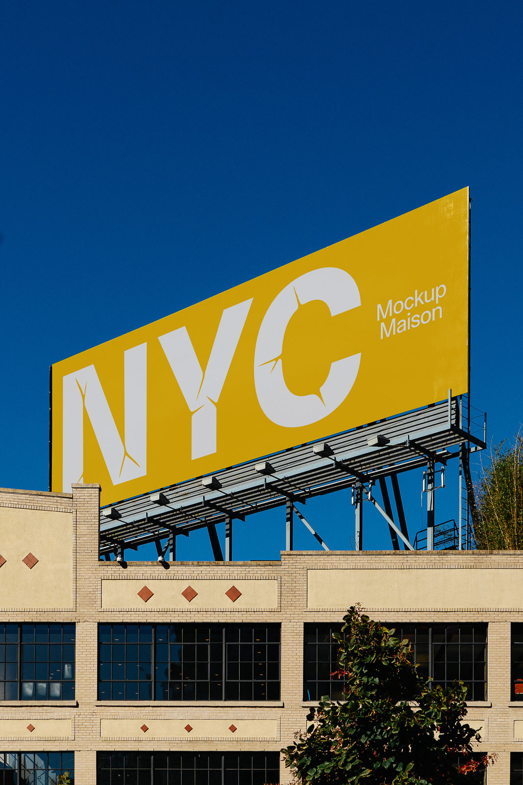 PSD mockup of a large billboard displaying "NYC" against a clear blue sky, mounted above a brick building with dark window panes.