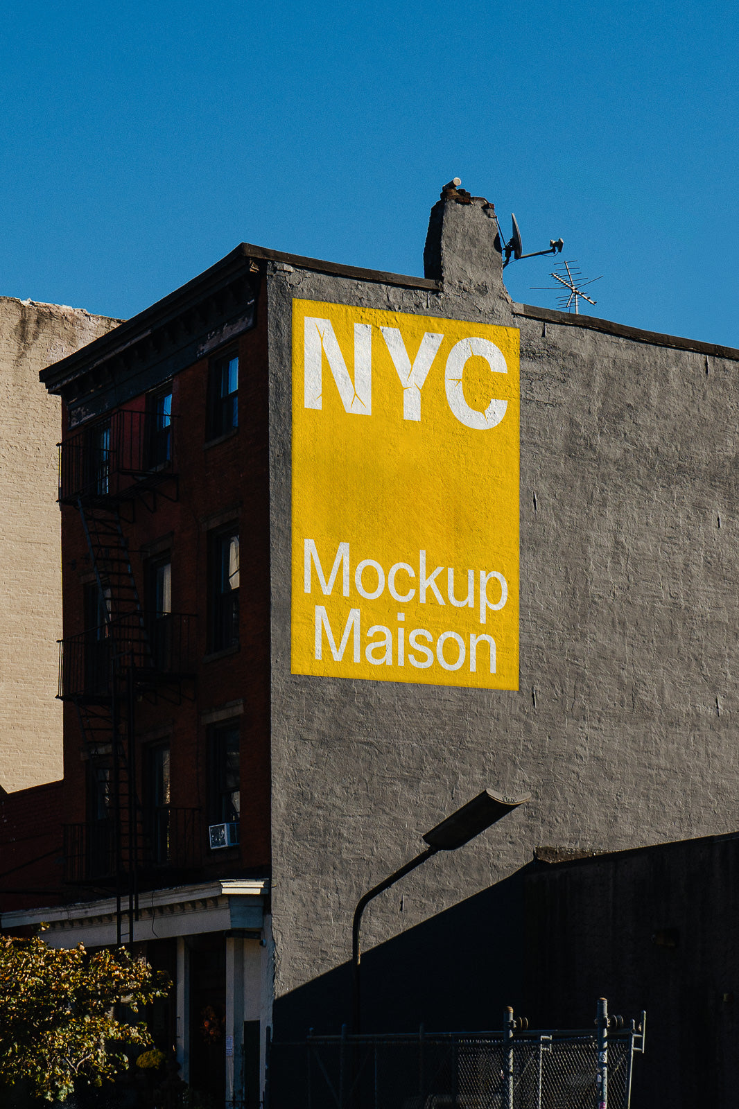 PSD mockup of a brick building facade featuring a large, vibrant yellow billboard with white text reading "NYC Mockup Maison."