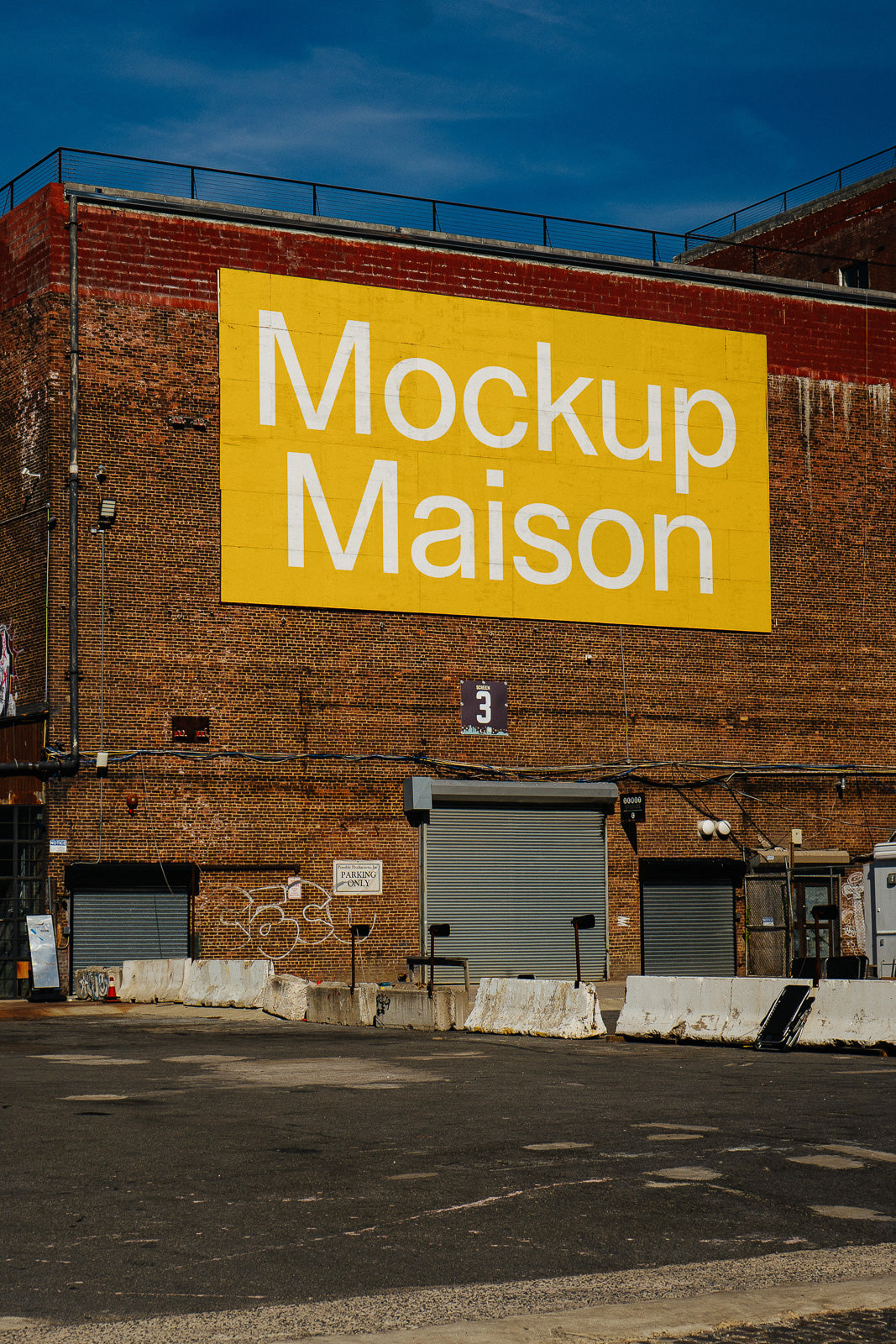PSD mockup of a large yellow sign with the words "Mockup Maison" on a brick building, viewed from a parking lot with barriers.