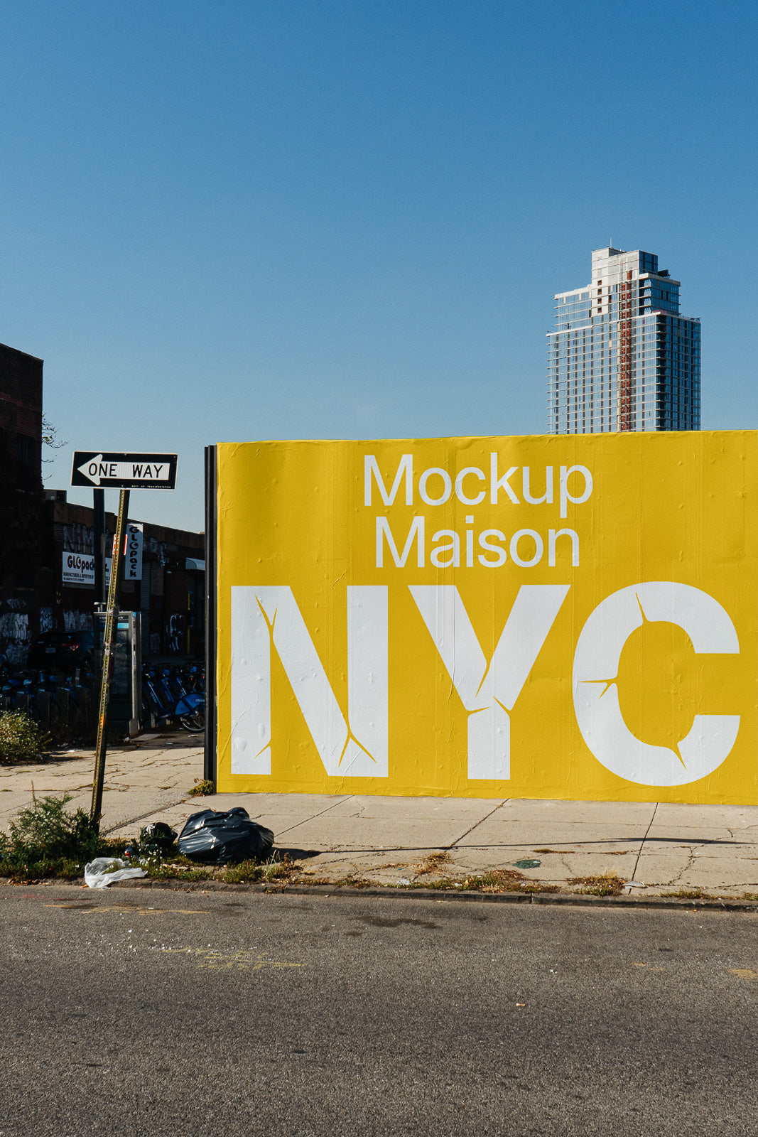 PSD mockup of a large yellow wall with bold white text "Mockup Maison NYC" next to a one-way street sign and tall building in background.