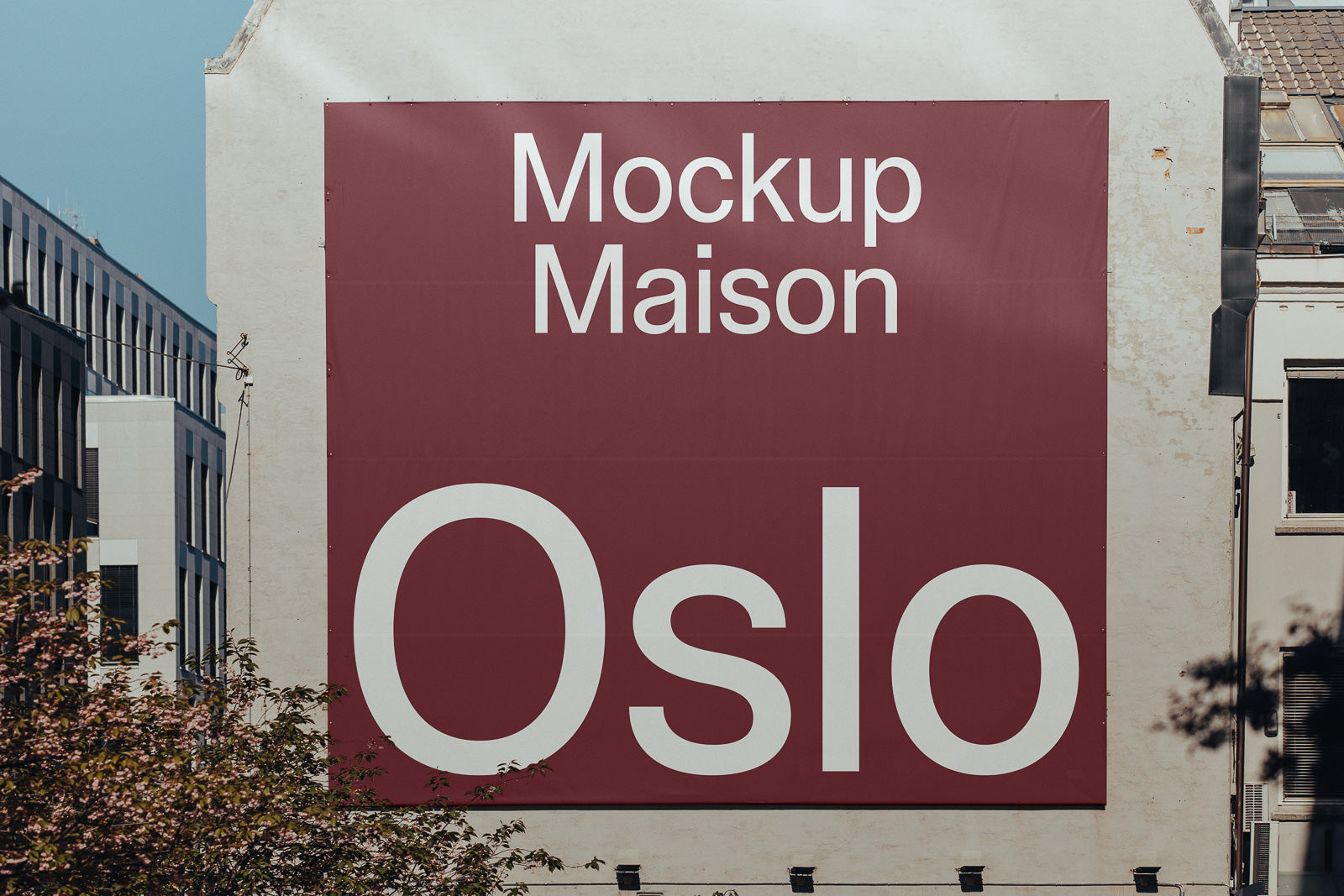 PSD mockup of a large outdoor wall with a maroon banner showcasing the text “Mockup Maison Oslo” in white, surrounded by urban buildings and trees.