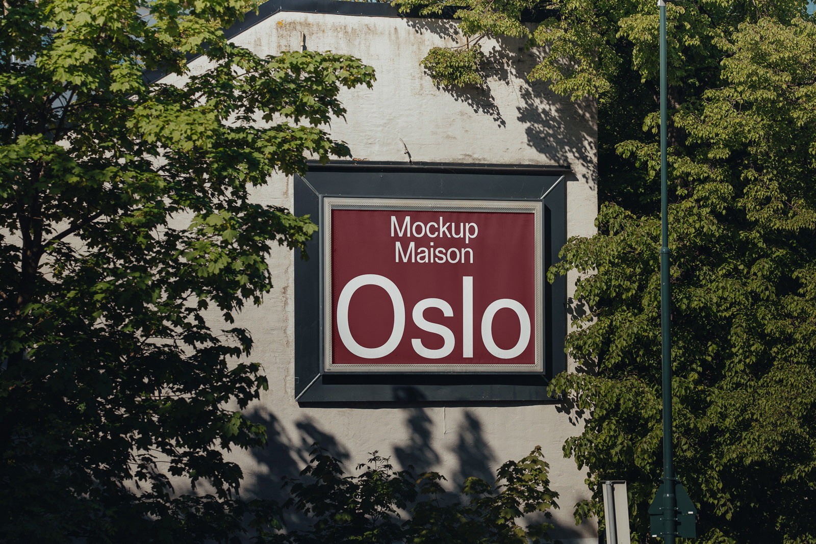 PSD mockup of a large red and white billboard displaying "Mockup Maison Oslo," set against a concrete building with green foliage surrounding the frame.