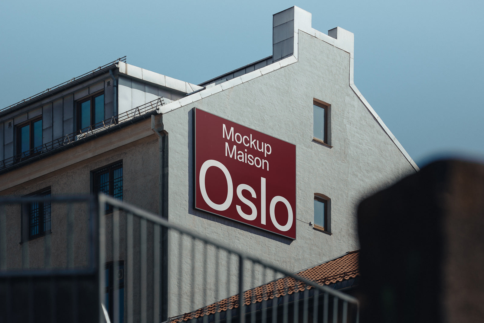 PSD mockup of a building facade with a large red and white sign displaying the text "Mockup Maison Oslo" against a clear blue sky.