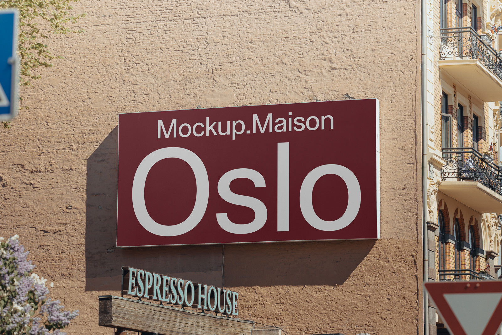 PSD mockup of a large red and white sign reading "Mockup.Maison Oslo" on a brick wall next to a building with balconies.