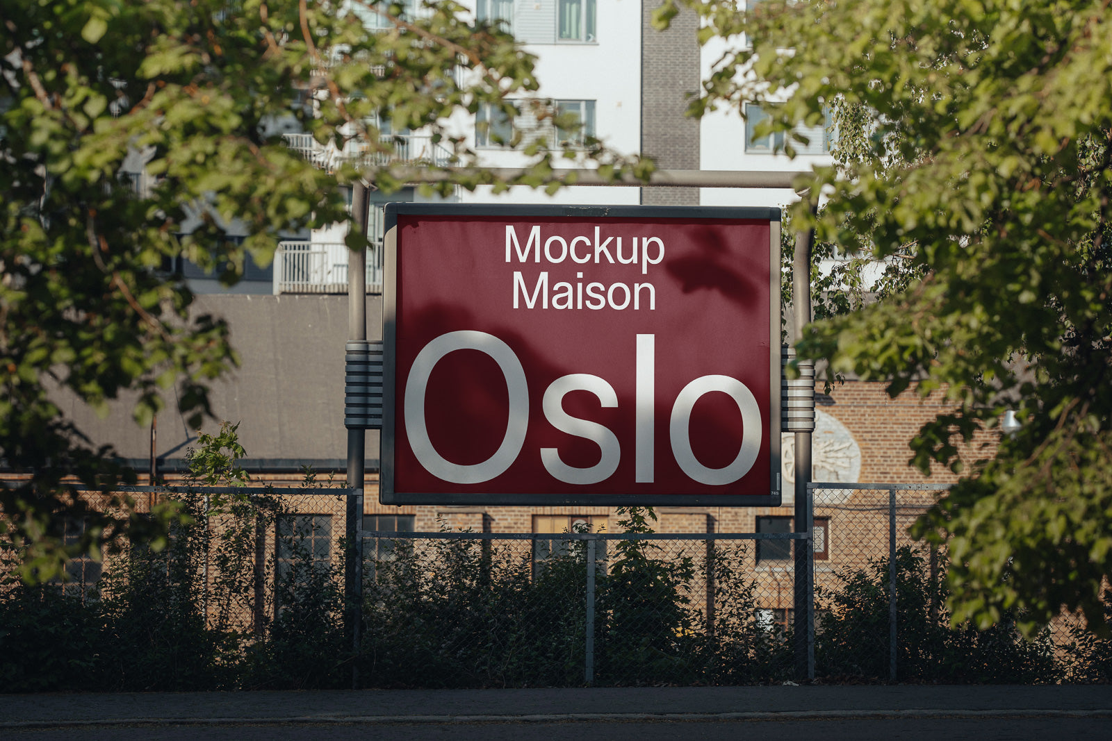 PSD mockup of a red sign displaying the text "Mockup Maison Oslo." The sign is surrounded by greenery and urban buildings in the background.