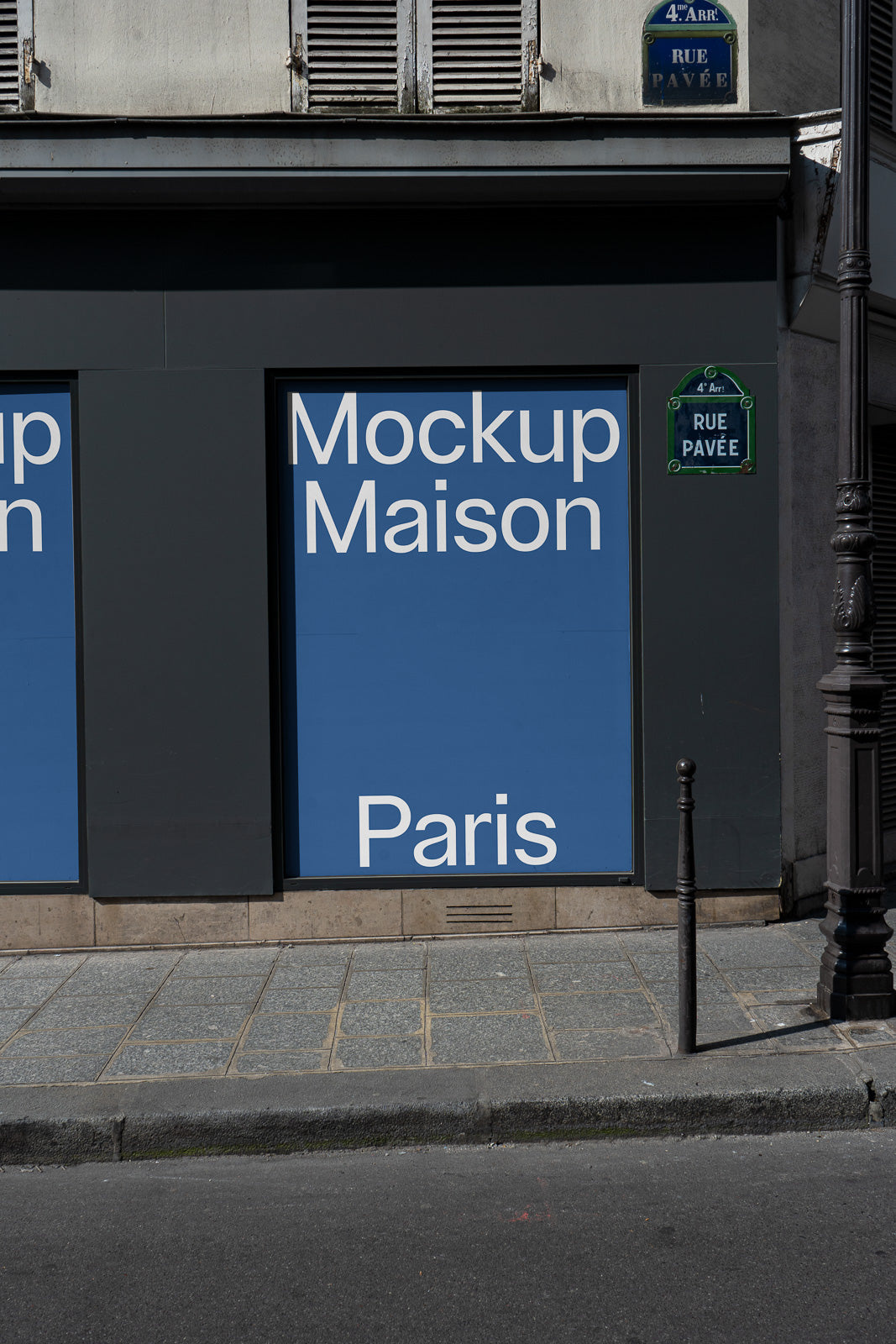 PSD mockup of a large blue poster with white text reading "Mockup Maison Paris" set against a dark building facade and a street sign.