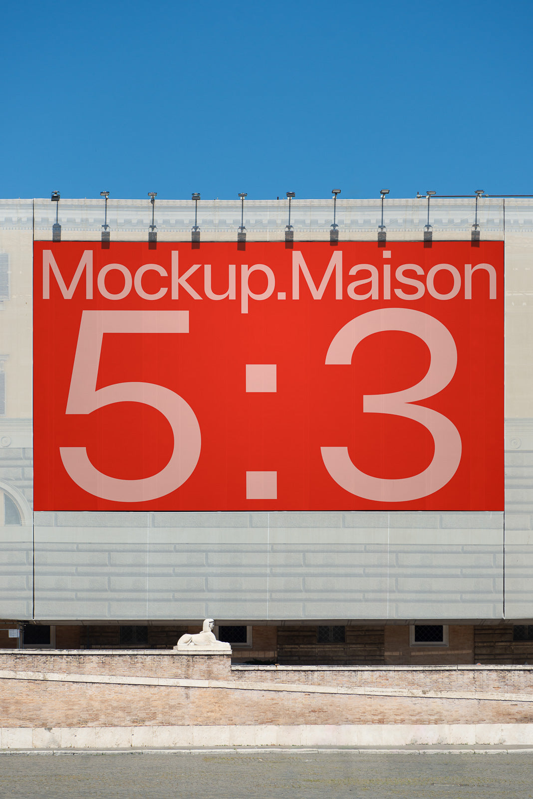 PSD mockup of a large outdoor banner displayed on a building, featuring a red and gray design with text "Mockup.Maison 5:3" against a clear blue sky.