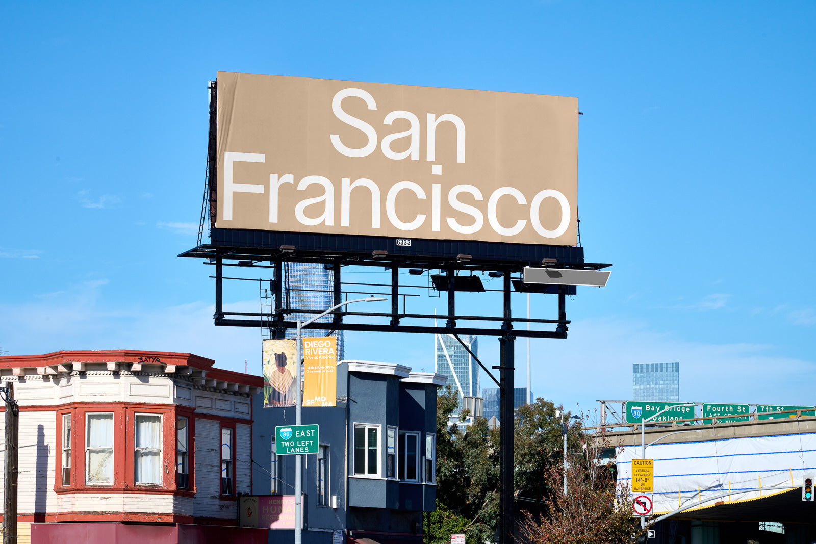 PSD mockup of a large outdoor billboard displaying "San Francisco" in bold white text against a tan background, situated above a city street.
