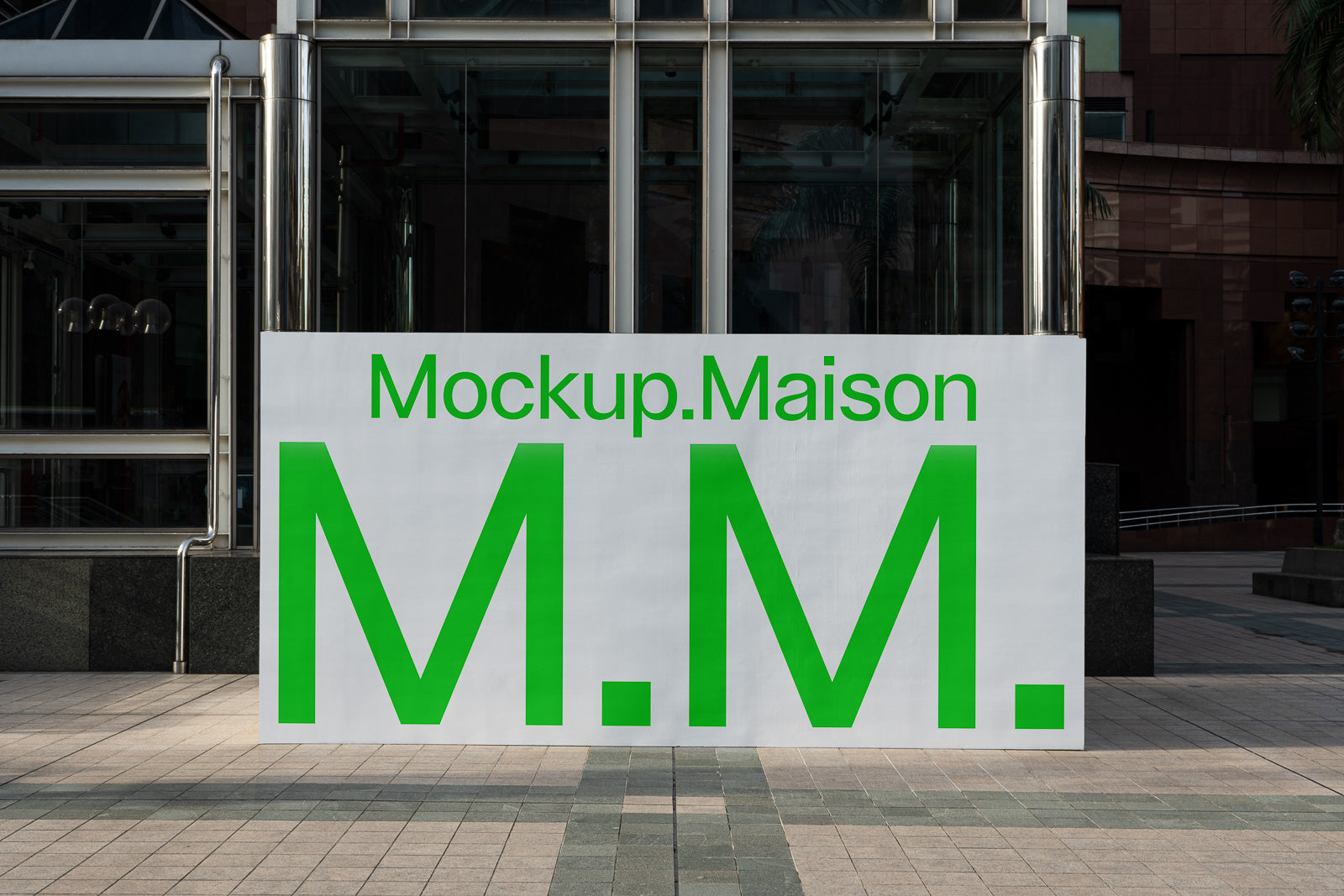 PSD mockup of a large outdoor sign displaying "Mockup.Maison M.M." in bold green text against a cityscape backdrop.