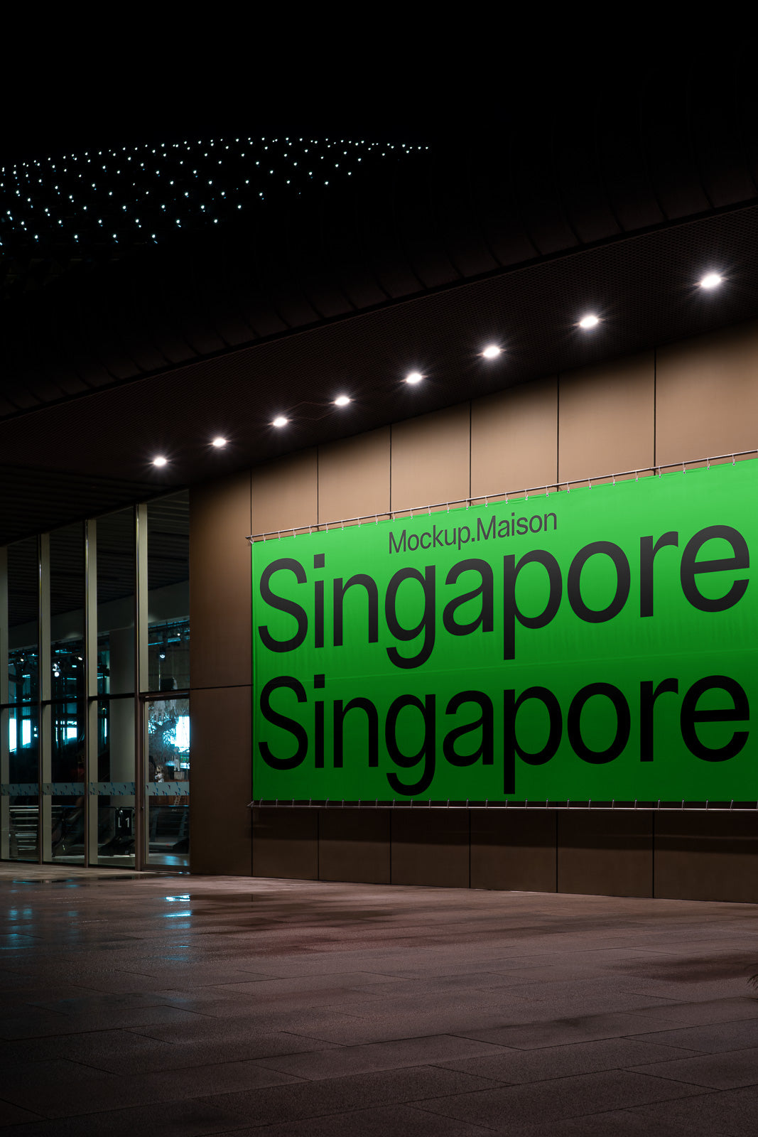 PSD mockup of a large green billboard on a building exterior at night, displaying the text "Mockup.Maison Singapore" in bold black letters.