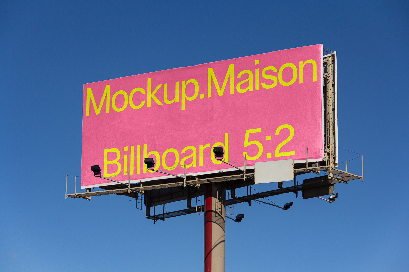 PSD mockup of a large billboard with a pink background and yellow text reading "Mockup.Maison Billboard 5:2" against a clear blue sky.