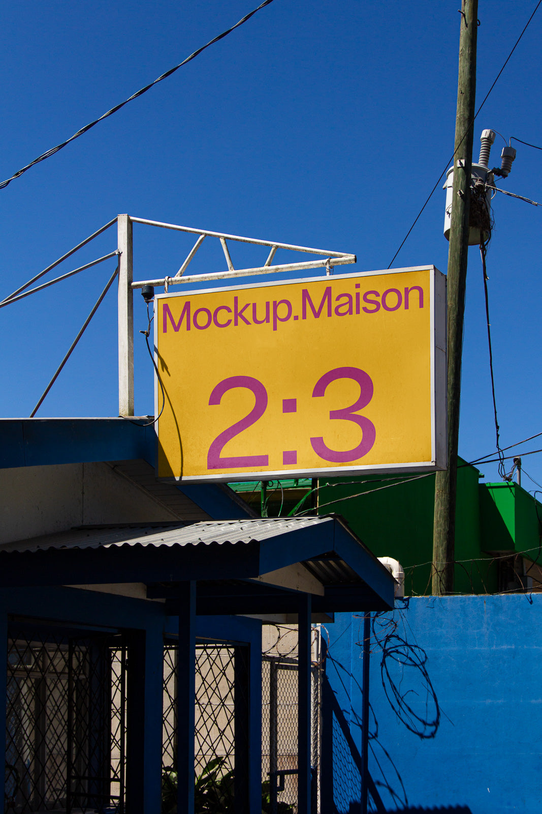PSD mockup of a yellow sign with "Mockup.Maison" and "2:3" in purple, mounted on a blue and metal structure against a clear sky.