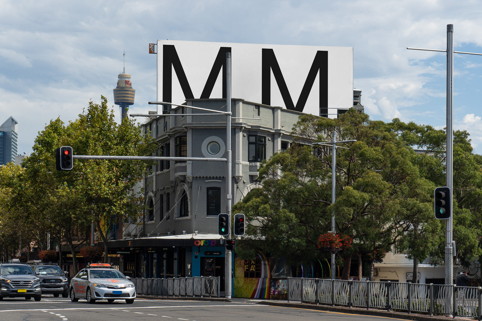 PSD mockup of a large billboard atop an urban building, surrounded by traffic lights and trees, showcasing a clear sky and city skyline in the background.