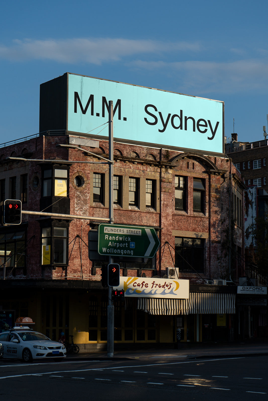 PSD mockup of a large urban billboard on top of a vintage brick building, situated at a busy street intersection with traffic signals.