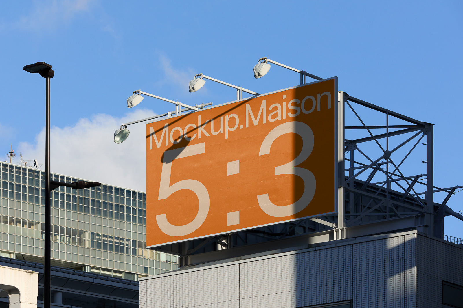 PSD mockup of a large outdoor billboard with an orange background displaying the text "Mockup.Maison 5:3" against a city backdrop.