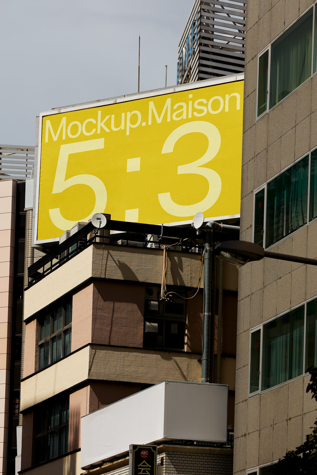 PSD mockup of a large yellow billboard on a building with text "Mockup.Maison 5:3" against a clear sky background.