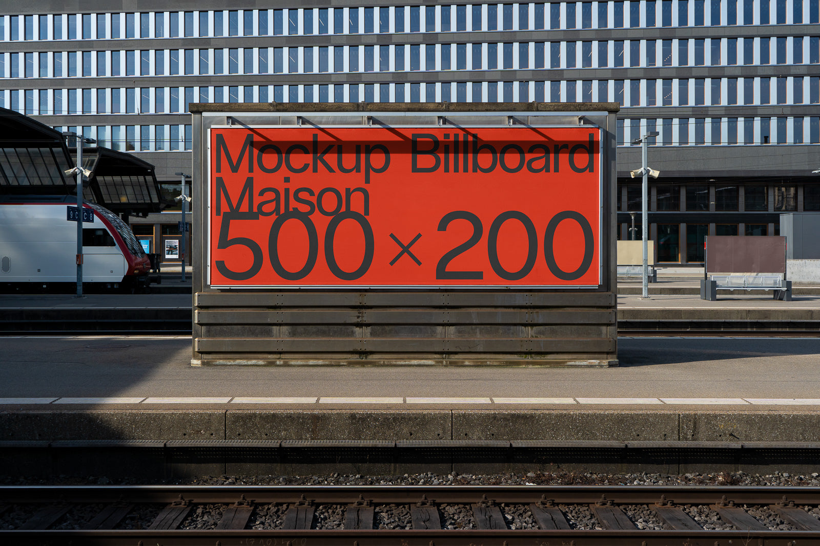 PSD mockup of a red billboard standing on a train station platform with the text "Mockup Billboard Maison 500 x 200" in bold black letters.