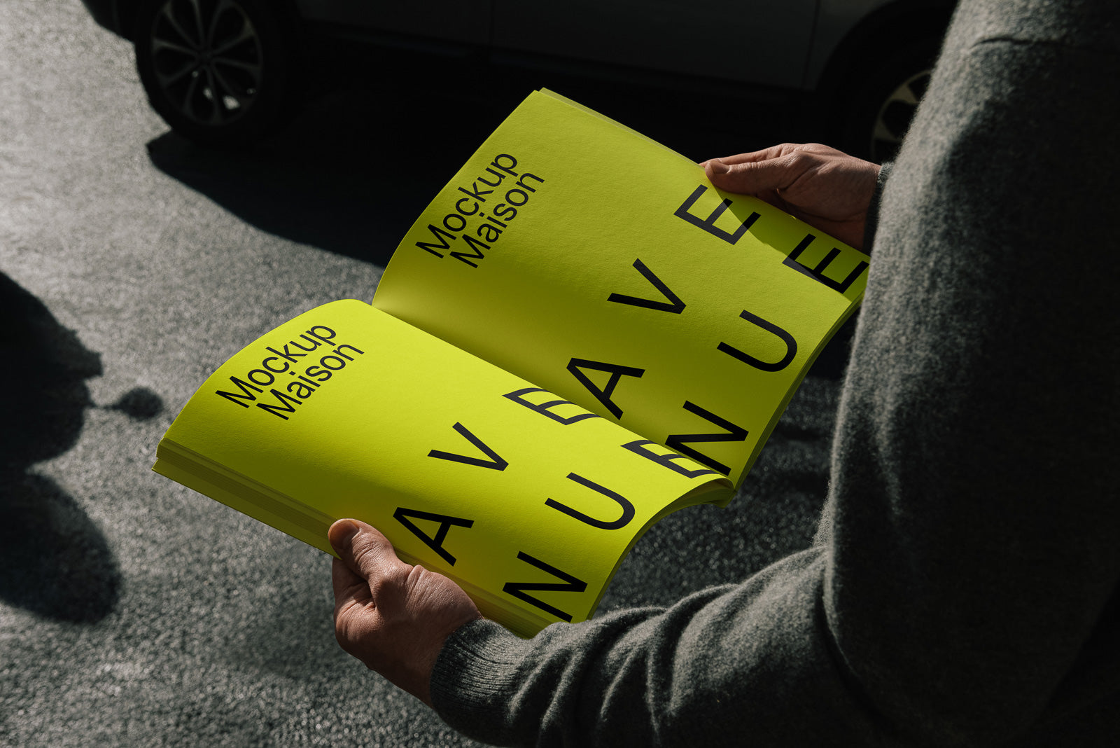 PSD mockup of a person holding an open, vibrant yellow booklet with bold black text "Mockup Maison" on a sunny day, showcasing pages outdoors.