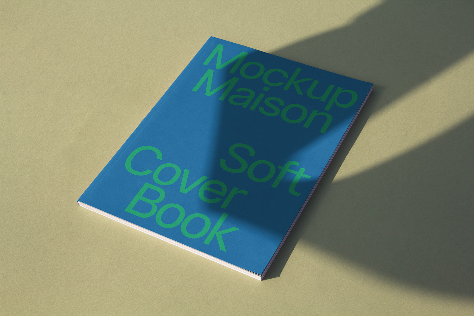 PSD mockup of a blue soft cover book on a light background, featuring large green text and partially covered by shadows.