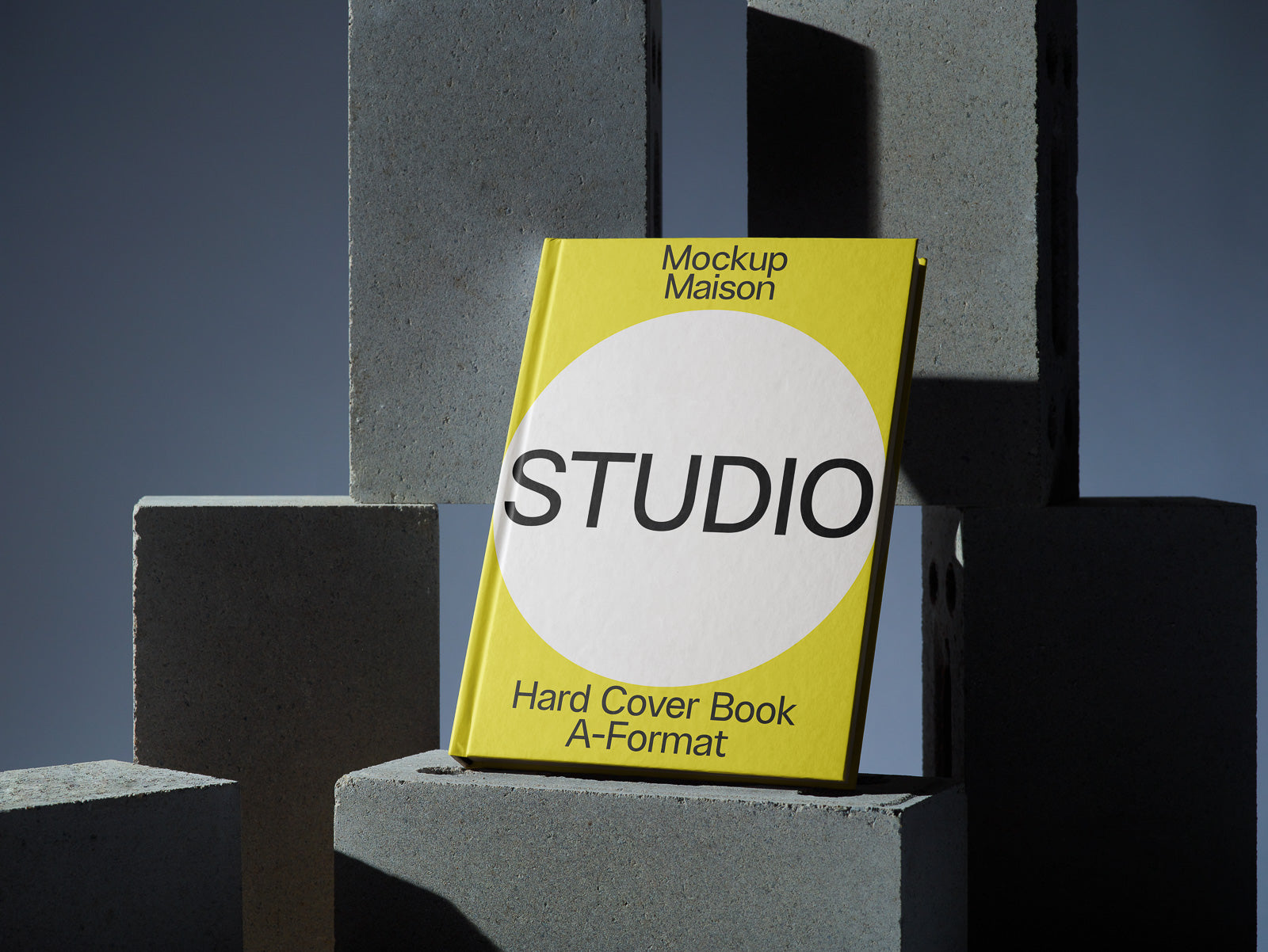 PSD mockup of a yellow hardcover book titled "Studio" with text "Mockup Maison" and "Hard Cover Book A-Format," set against stacked gray blocks.