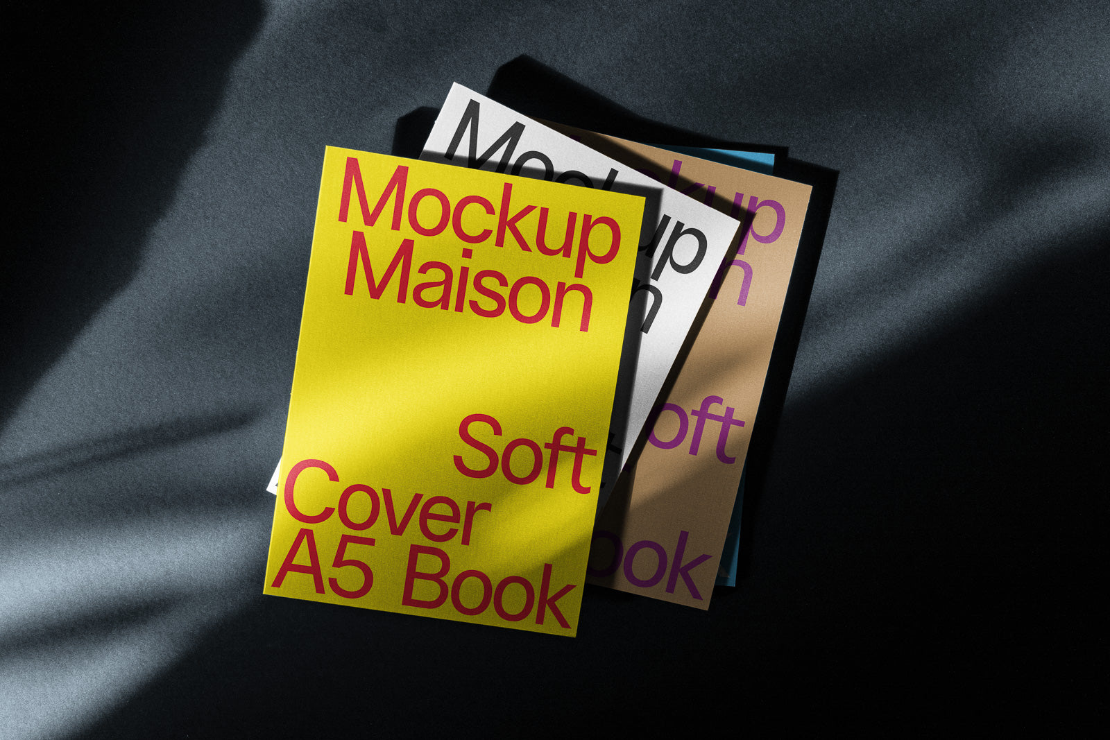 PSD mockup of stacked A5 soft cover books with bold, colorful typography on a dark background with dramatic lighting.