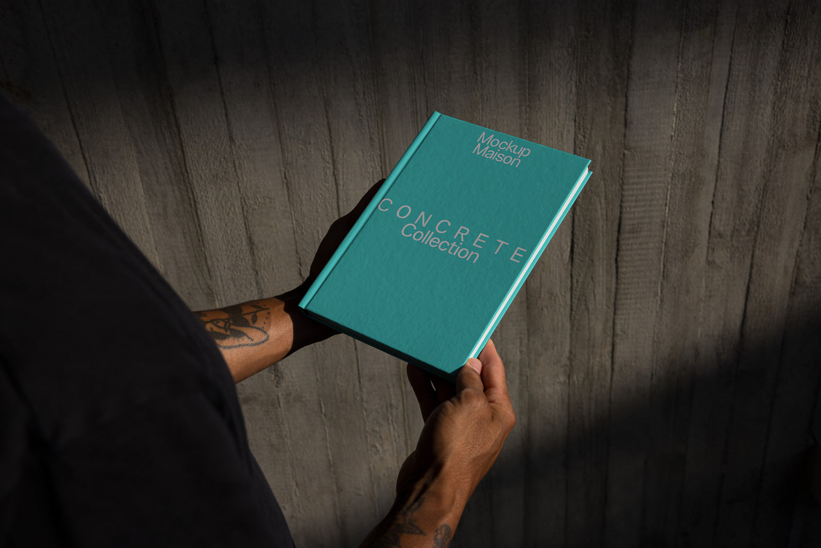 PSD mockup of a person holding a turquoise hardcover book titled "Concrete Collection" against a textured concrete wall.
